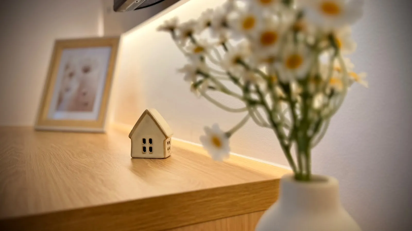 O căsuță de lemn și o vază cu margarete pe un raft, într-un apartament HUBIX Renting